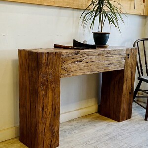 May include: A rustic wooden console table with a natural wood finish. The table has a simple design with a rectangular top and two legs. The table is made of reclaimed wood and has a unique character.