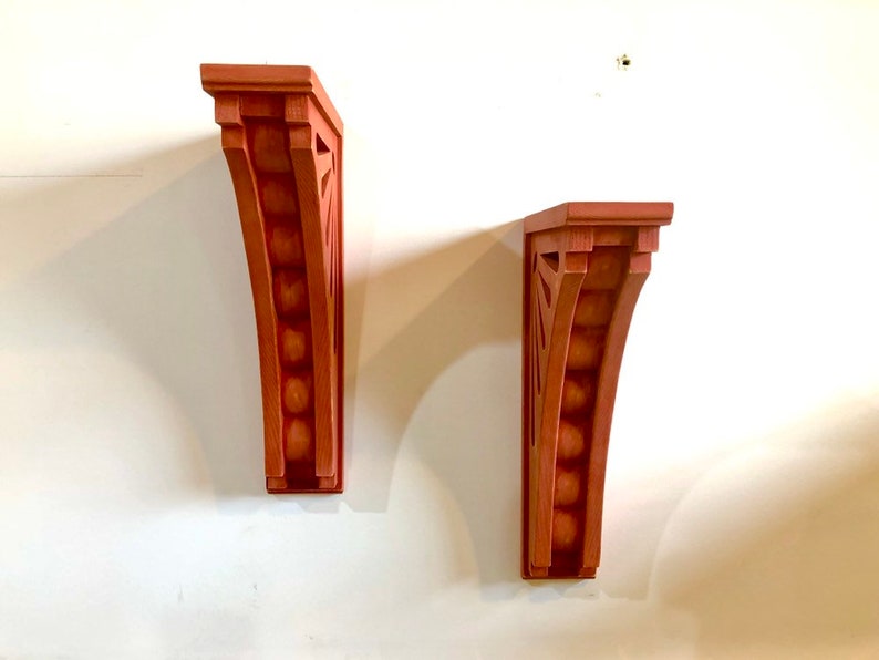 May include: Two wooden wall brackets with a decorative design. The brackets are painted a reddish-brown color and have a curved shape.