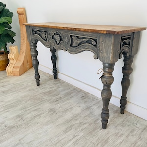 Peut inclure: Une console en bois gris avec des d&eacute;tails sculpt&eacute;s et des pieds tourn&eacute;s. La table a une finition vieillie et un plateau rectangulaire.