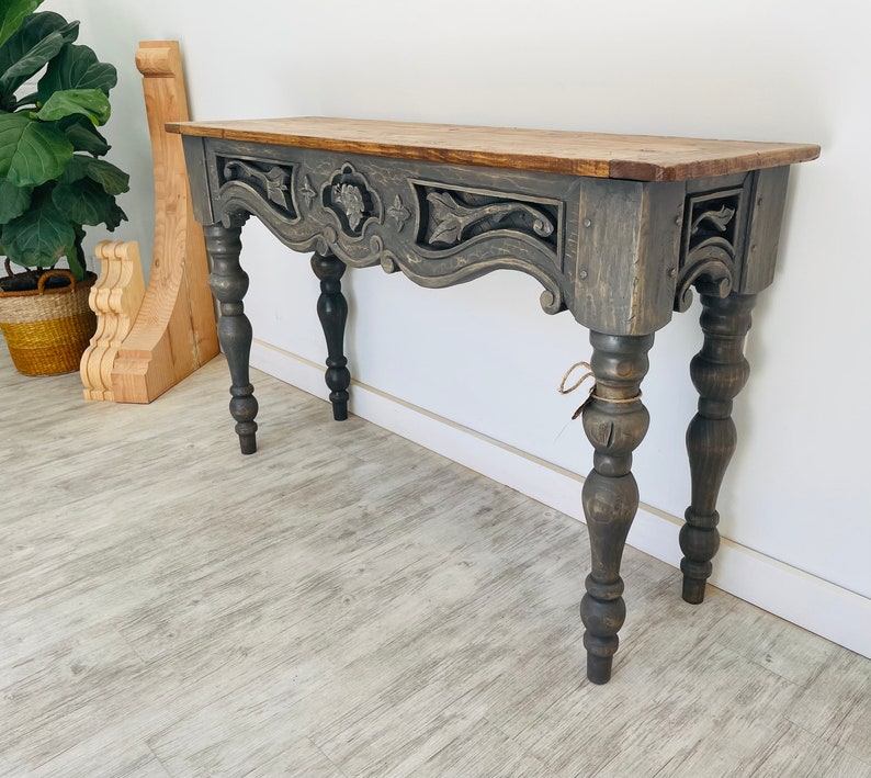 Peut inclure: Une console en bois gris avec des d&eacute;tails sculpt&eacute;s et des pieds tourn&eacute;s. La table a une finition vieillie et un plateau rectangulaire.