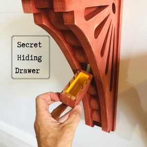 May include: A red wooden wall shelf with a secret hiding drawer. The drawer is open and reveals a yellow interior. The text "Secret Hiding Drawer" is written on a white background.