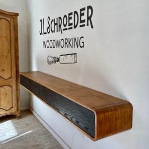May include: A wall-mounted wooden shelf with a curved edge and three black drawers. The shelf is labeled "J.L. SCHROEDER WOODWORKING".