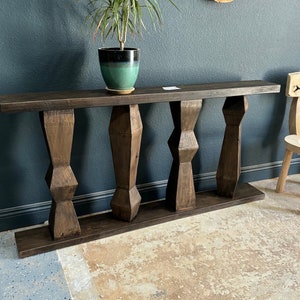 May include: A dark brown wooden console table with four turned legs. The table has a rectangular top and a simple design.