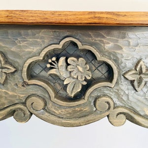 Peut inclure: Un plateau de table en bois gris fonc&eacute; avec des d&eacute;tails sculpt&eacute;s complexes. Les sculptures pr&eacute;sentent un motif floral sur fond de treillis. Le plateau de table a une finition vieillie.