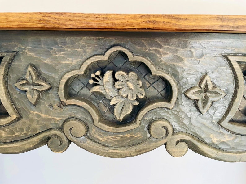 Peut inclure: Un plateau de table en bois gris fonc&eacute; avec des d&eacute;tails sculpt&eacute;s complexes. Les sculptures pr&eacute;sentent un motif floral sur fond de treillis. Le plateau de table a une finition vieillie.