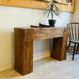 May include: A rustic wooden console table with a thick, reclaimed wood top and two sturdy legs. The table has a natural wood finish and shows signs of age and wear.