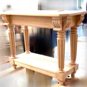 May include: A light wood console table with a simple design and four fluted legs. The table has a shelf underneath the top surface.