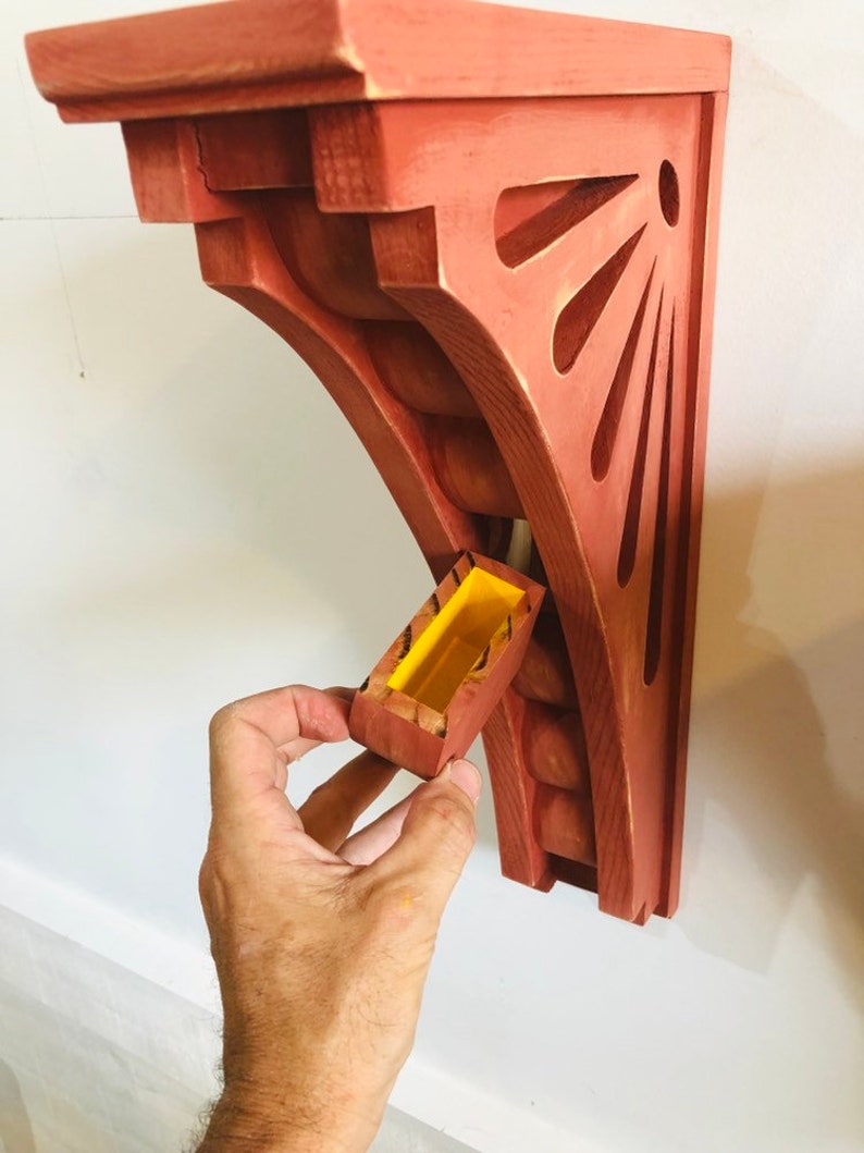 May include: A red wooden shelf bracket with a decorative cutout design and a small yellow box attached to the side.