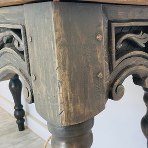 Peut inclure: Gros plan sur une table en bois gris fonc&eacute; avec des d&eacute;tails sculpt&eacute;s et des pieds tourn&eacute;s. La table a une finition vieillie et semble &ecirc;tre antique.