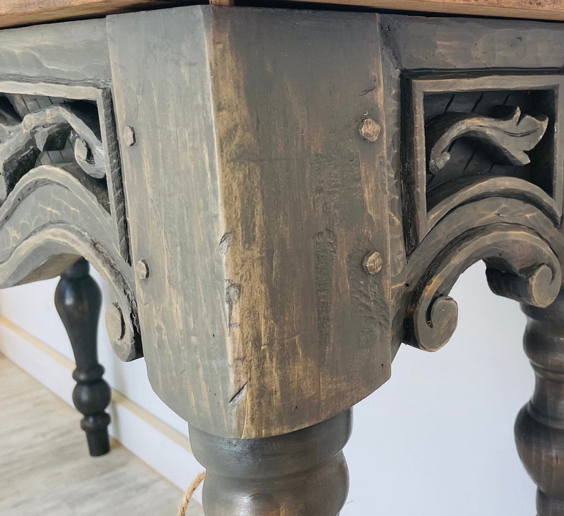 Peut inclure: Gros plan sur une table en bois gris fonc&eacute; avec des d&eacute;tails sculpt&eacute;s et des pieds tourn&eacute;s. La table a une finition vieillie et semble &ecirc;tre antique.