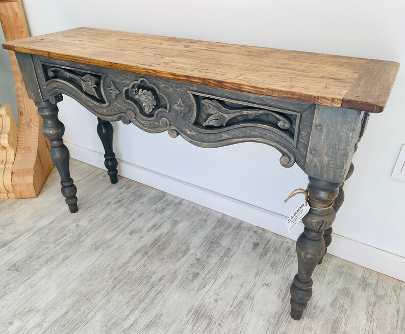 Peut inclure: Une console grise avec un motif en bois sculpt&eacute; et un plateau en bois naturel. La table a des pieds tourn&eacute;s et une finition vieillie.