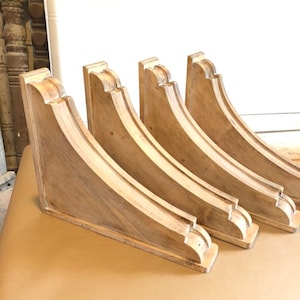 May include: Four wooden corbels with a distressed white paint finish. The corbels are curved and have a decorative design.