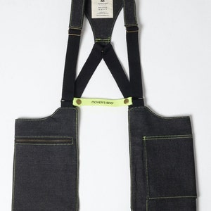 May include: A black denim chest rig with two pockets on the front and adjustable straps. The straps are black with yellow stitching and have a yellow label that reads "MOVER'S BAG".