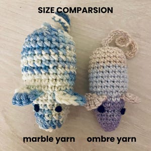 May include: Two crocheted toys, one larger and one smaller, in a side-by-side comparison. The larger toy is blue and white marble yarn, and the smaller toy is ombre yarn in shades of purple and blue. The text "SIZE COMPARISON" is at the top.