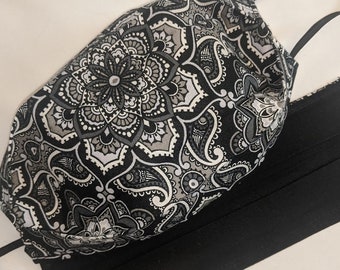 May include: Two face masks. One mask features a black, white, and gray paisley pattern. The other mask is solid black. Both masks have black elastic ear loops. The masks are designed for face protection.