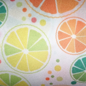 Könnte beinhalten: Ein weißer Stoff mit einem sich wiederholenden Muster aus bunten Zitrusfrüchtescheiben. Die Fruchtscheiben sind in Grün-, Gelb-, Orange- und Rosatönen gehalten. Der Hintergrund ist weiß mit kleinen weißen Punkten.