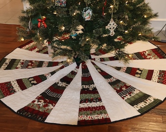 May include: A white quilted Christmas tree skirt with a black trim. The skirt has a patchwork design with red, green, and black fabric. The skirt is decorated with a variety of Christmas patterns.