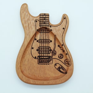 May include: A wooden guitar-shaped dish with a burnt-in design of a guitar. The dish is made of light brown wood and has a smooth surface.