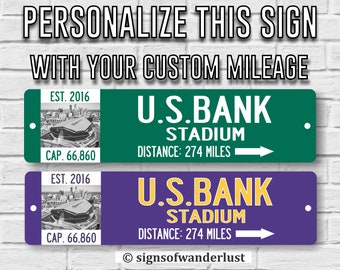 May include: Two personalized metal signs with a green and purple background. The signs feature a black and white photo of U.S. Bank Stadium, the text "U.S. BANK STADIUM", "EST. 2016", "CAP. 66,860", and "DISTANCE: 274 MILES".