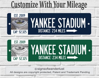 May include: Two rectangular signs with the text "YANKEE STADIUM" and "DISTANCE: 234 MILES". One sign is navy blue, the other is green. Both signs have an image of the stadium, the text "EST. 2009" and "CAP. 52,325". The top text says "Customize With Your Mileage".