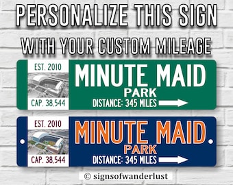 May include: Two personalized street signs with a green and blue background. The signs feature the text "Minute Maid Park" and the text "EST. 2010 CAP. 38,544 DISTANCE: 345 MILES". The signs also feature a small image of a baseball stadium.
