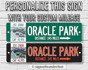 May include: Two rectangular metal signs featuring the text ORACLE PARK, DISTANCE: 345 MILES, and a directional arrow. Each sign includes an aerial photograph of a stadium, the text EST. 2000, and CAP. 41,915. One sign is green, the other is black.