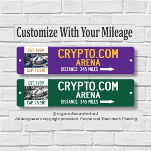 May include: Two rectangular signs with the text "Customize With Your Mileage" above them. The signs read "CRYPTO.COM ARENA" with a distance of 345 miles. One sign is purple, the other is green. The signs are on a white brick wall.