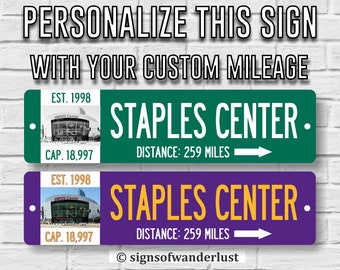 May include: Two personalized street signs with a purple and green background. The signs feature a picture of the Staples Center in Los Angeles, California. The text on the signs reads "STAPLES CENTER" with the distance in miles. The signs are customizable with your own mileage.