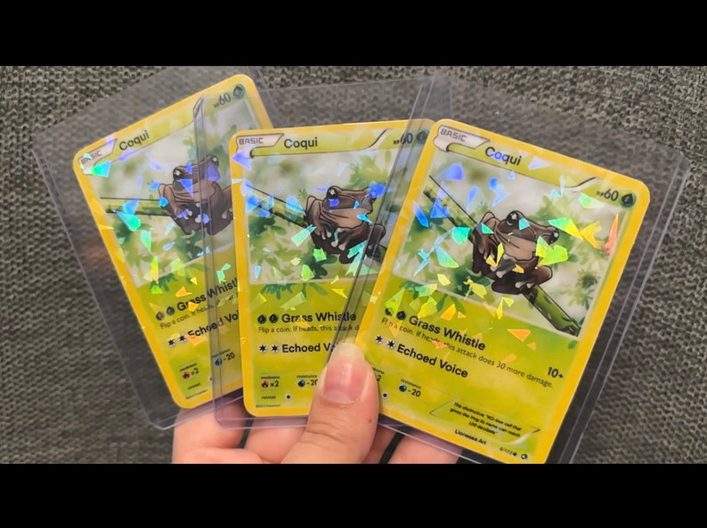 K&ouml;nnte beinhalten: Drei holografische Pokemon-Sammelkarten mit einem gr&uuml;nen Froschcharakter namens "Coqui". Die Karten sind gelb mit gr&uuml;nen und braunen Akzenten. Die Karten haben den Text "Grass Whistle" und "Echoed Voice" auf sich.