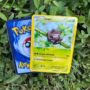K&ouml;nnte beinhalten: Eine Pokemon-Sammelkarte mit einem gr&uuml;nen Frosch mit braunen Flecken auf einem gr&uuml;n-braunen Hintergrund. Die Karte tr&auml;gt den Titel "Coqui" und hat 60 KP. Die Karte hat zwei Attacken: "Grass Whistle" und "Echoed Voice".