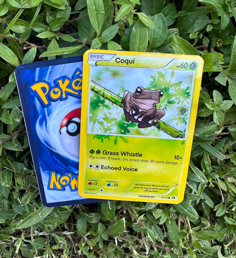 K&ouml;nnte beinhalten: Eine Pokemon-Sammelkarte mit einem gr&uuml;nen Frosch mit braunen Flecken auf einem gr&uuml;n-braunen Hintergrund. Die Karte tr&auml;gt den Titel "Coqui" und hat 60 KP. Die Karte hat zwei Attacken: "Grass Whistle" und "Echoed Voice".