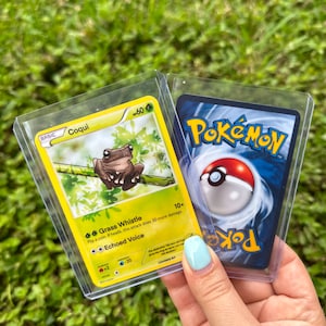 K&ouml;nnte beinhalten: Zwei Pok&eacute;mon-Sammelkarten, eine mit einem gr&uuml;nen Frosch mit dem Text "BASIC Coqui 60" und die andere mit einem roten und wei&szlig;en Pok&eacute;ball mit dem Text "Pokemon".