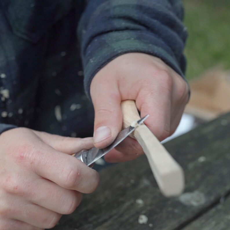 May include: A person's hands are shown carving a piece of wood with a small knife. The wood is light brown and the knife is silver.