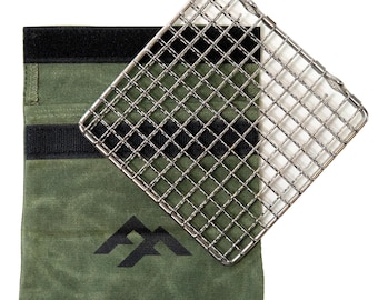 May include: A square stainless steel wire grill grate positioned diagonally over a rectangular olive green canvas pouch. The pouch features a black hook-and-loop closure strip at the top and a black geometric mountain-shaped logo printed on the front.