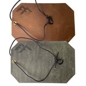 May include: Two leather keychains with a mountain peak logo and a black cord with a metal clasp. The keychain on top is brown and the keychain on the bottom is gray.