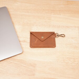 May include: A brown leather wallet with a flap closure and a metal clasp. The wallet has a small pocket on the front and a key ring attached to the side.