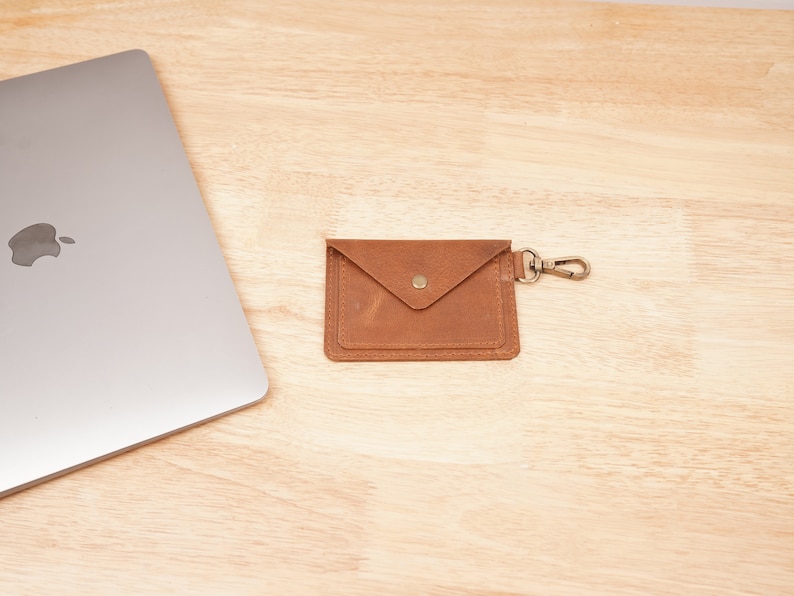 May include: A brown leather wallet with a flap closure and a metal clasp. The wallet has a small pocket on the front and a key ring attached to the side.