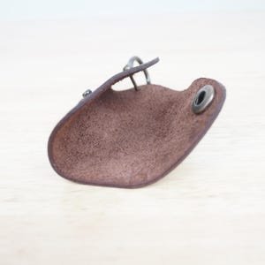 May include: A brown leather key holder with a metal ring and a snap closure. The key holder is open and the inside is visible.