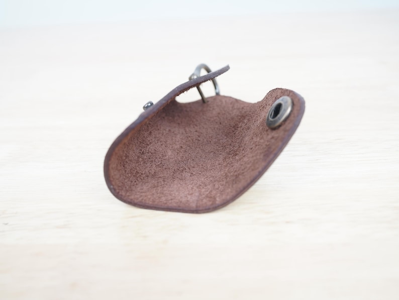 May include: A brown leather key holder with a metal ring and a snap closure. The key holder is open and the inside is visible.