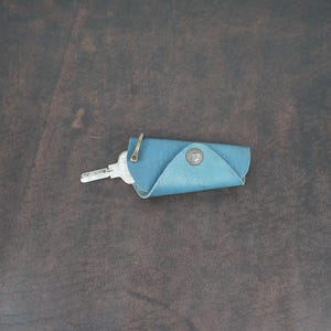 May include: A blue leather key holder with a metal ring and a key inside.