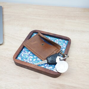 May include: A brown leather wallet and keys on a blue and white patterned ceramic tray with a wooden frame.