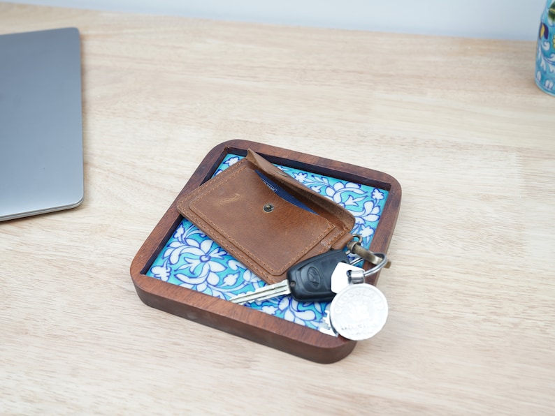 May include: A brown leather wallet and keys on a blue and white patterned ceramic tray with a wooden frame.