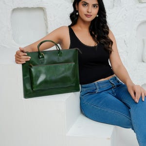 Op de afbeelding: Een groene leren tote bag met een bijpassend kleiner etui. De tote heeft een handvat aan de bovenkant en een ritssluiting. De tas heeft een diepgroene kleur. De achtergrond is wit.