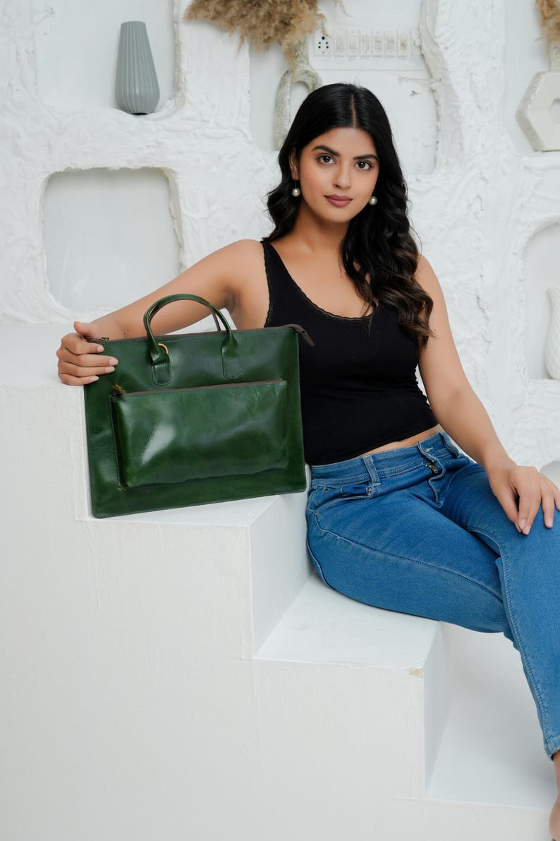 Op de afbeelding: Een groene leren tote bag met een bijpassend kleiner etui. De tote heeft een handvat aan de bovenkant en een ritssluiting. De tas heeft een diepgroene kleur. De achtergrond is wit.