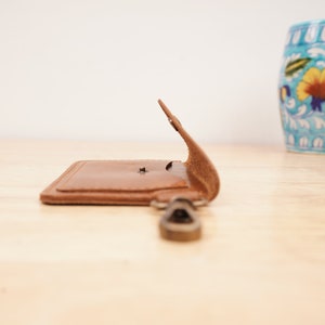 May include: A brown leather key chain with a metal ring and a small flap that opens to reveal a pocket.
