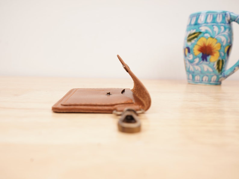 May include: A brown leather key chain with a metal ring and a small flap that opens to reveal a pocket.