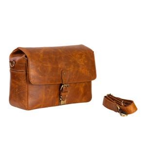 May include: A brown leather messenger bag with a flap closure and a buckle. The bag has a shoulder strap and a distressed finish. The bag is rectangular and has a vintage look.