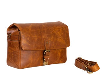 May include: A brown leather messenger bag with a flap closure and a buckle. The bag has a shoulder strap and a distressed finish. The bag is rectangular and has a vintage look.