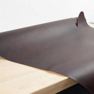 May include: A roll of dark brown leather, unfurled on a wooden surface.