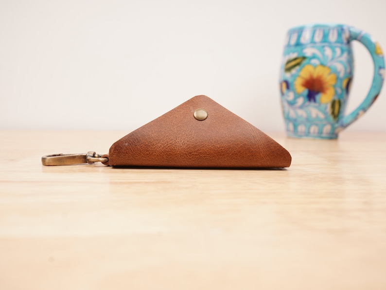 May include: A brown leather triangle-shaped key chain with a metal clasp and a button closure.